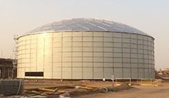 Large Glass-Fused-to-Steel tank with an aluminum geodesic dome roof under construction at an industrial worksite.