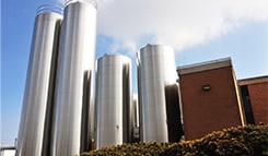 A group of commercial stainless steel tanks and silos for liquid storage, installed outdoors at a modern industrial facility.