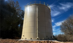 Tan bolted steel fire protection water storage tank with exterior standpipe and roof railing for commercial fire suppression systems.